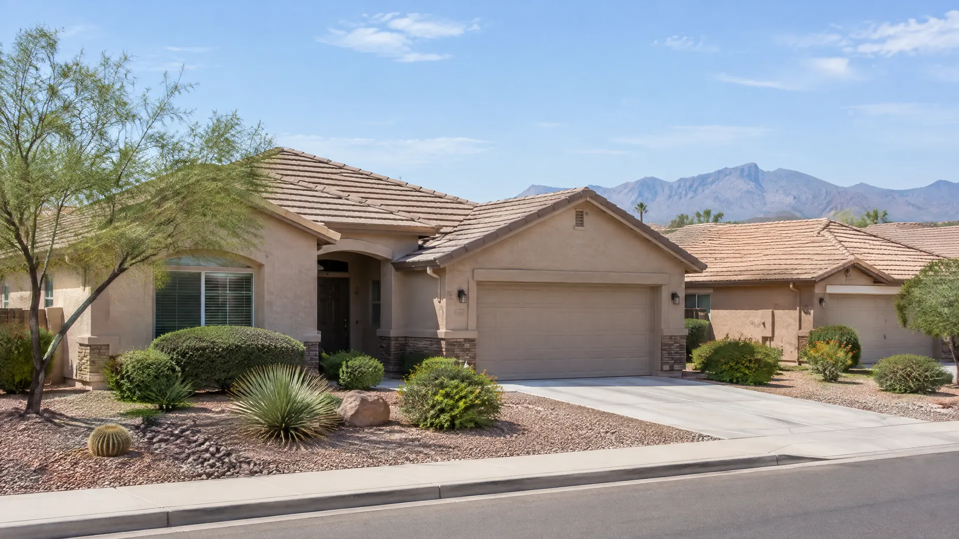 Single-story stucco homes with tan concrete tile roofs and rock front yards in an east Chandler neighborhood, mountains faint in the distance