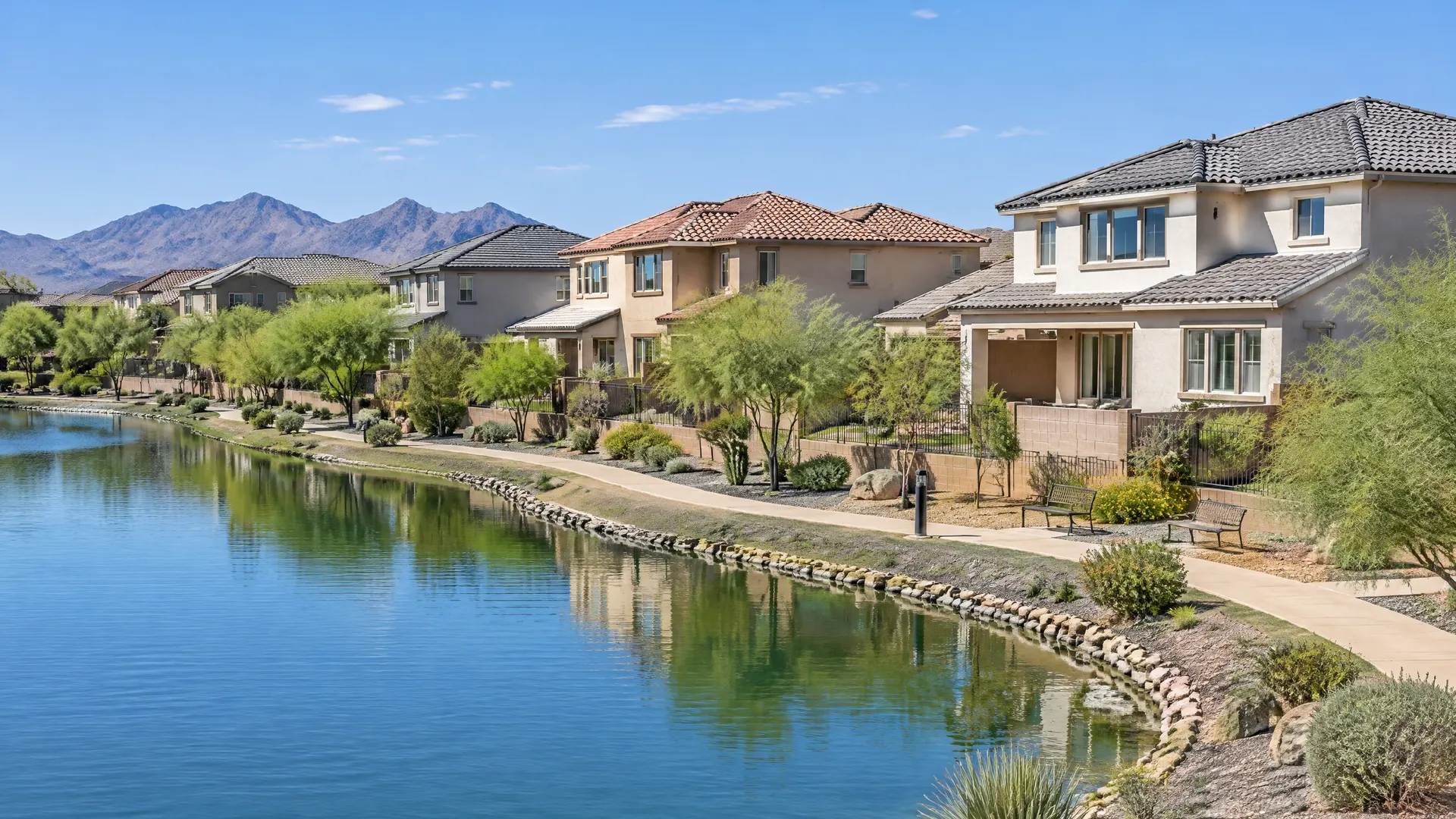 Newer two-story homes with varied concrete tile roof colors beside a small community lake with a walking path in Chandler