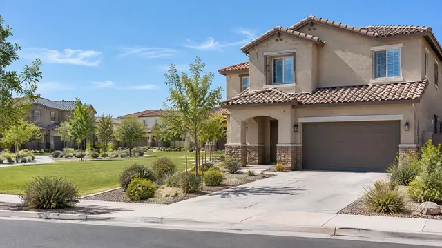 Two-story stucco homes with barrel concrete tile roofs in a south Chandler master-planned community, green common area, young trees and blue sky