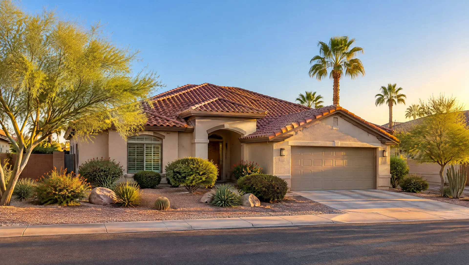 Wide street-level view of a single-story stucco home in Chandler with a newly replaced terracotta-colored S-shaped concrete tile roof, crisp ridge lines, palm and palo verde trees, desert front yard and a clear blue sky at golden hour